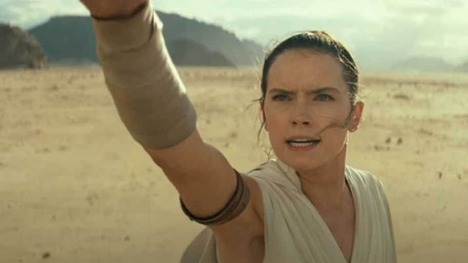 Rey from Star Wars extends arm upward, focused expression, in desert setting