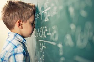 Boy resting head against chalkboard with math equations, expressing confusion or frustration