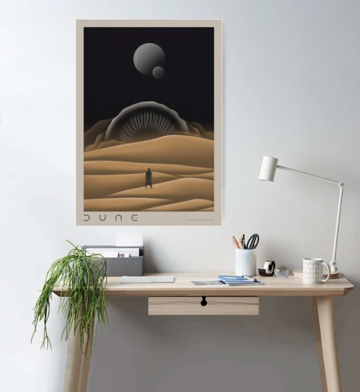 Poster of &quot;Dune&quot; film with minimalist desert scene and figure, hung above a tidy desk setup