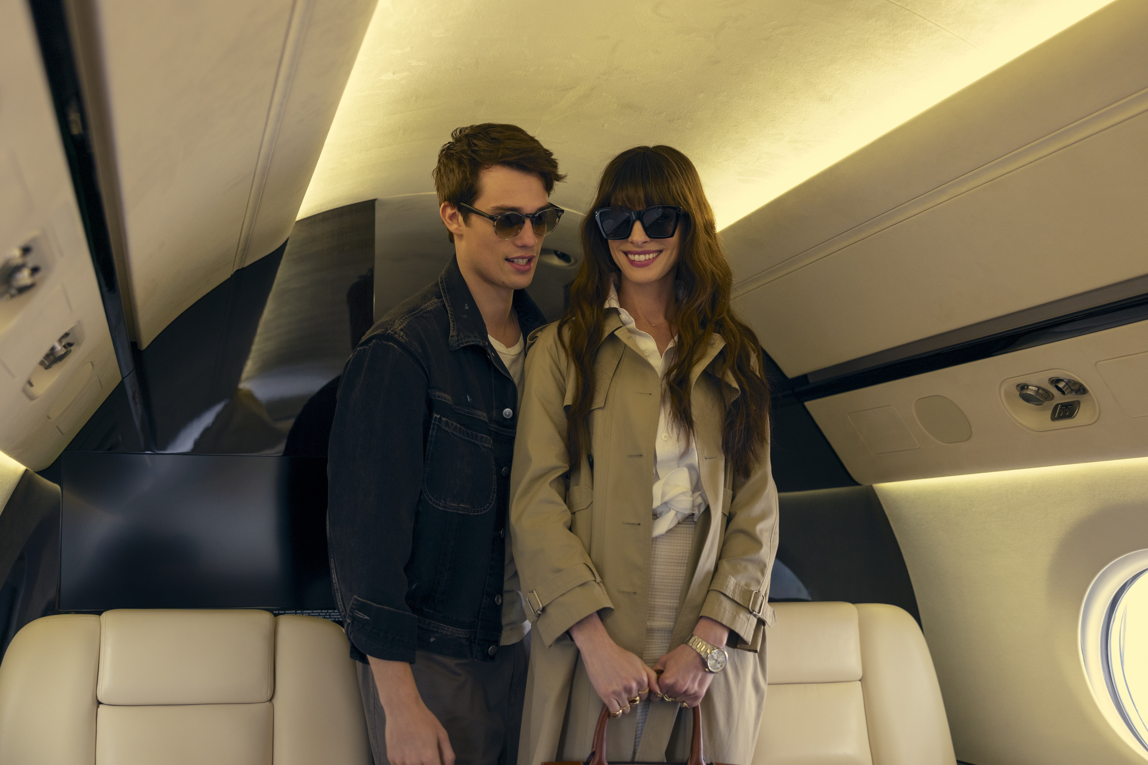 Two people standing inside an airplane cabin, smiling, dressed in casual chic attire