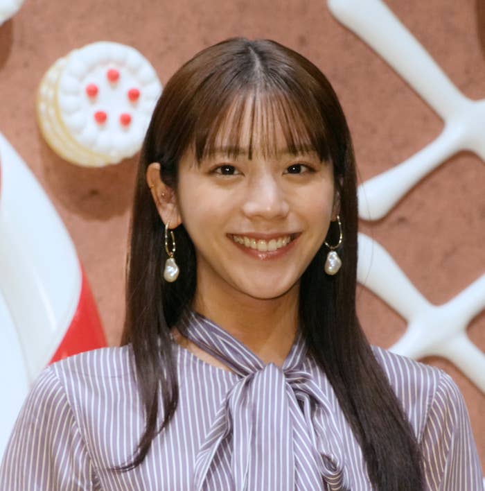 女性が笑顔でカメラを見つめ、ストライプのブラウスとピアスを着用しています。