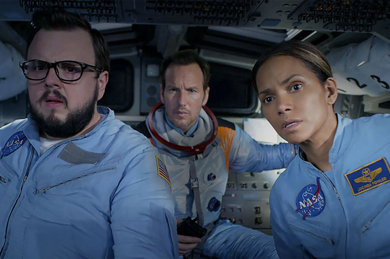 Three actors in a spacecraft cockpit, looking concerned. They are wearing space suits with NASA patches