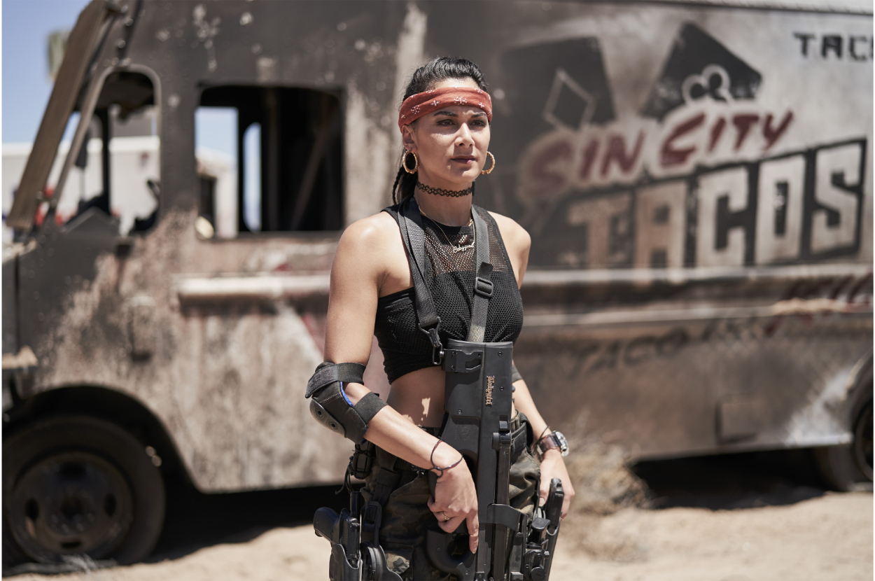 Woman in black outfit with arm bracers stands by &quot;Sin City Tacos&quot; truck