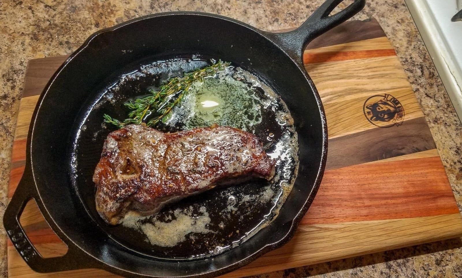 Sepotong steak yang lezat dimasak dalam wajan besi cor dengan setangkai herba segar dan sepotong mentega cair