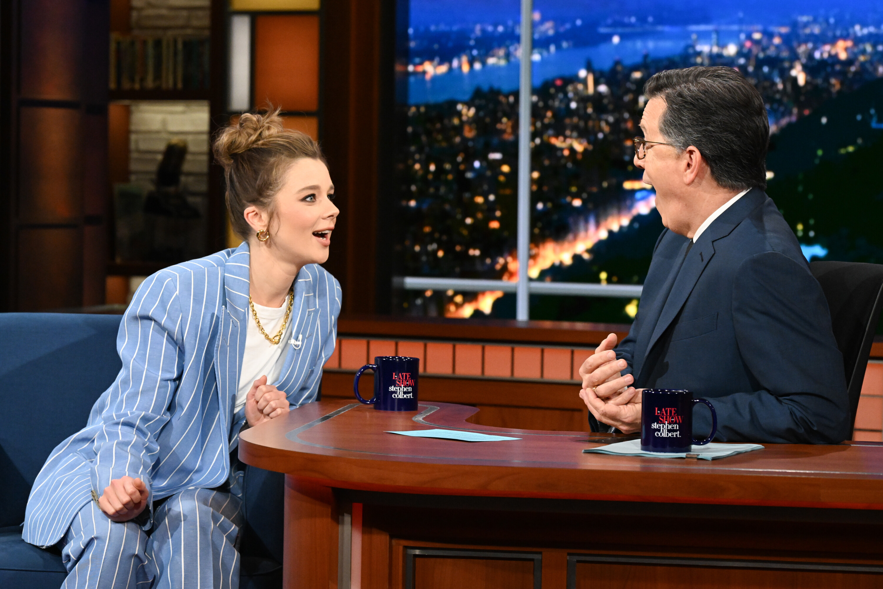 Claudia Jessie, in a striped suit, enthusiastically converses with Stephen Colbert, in a suit, during an interview on "The Late Show with Stephen Colbert."