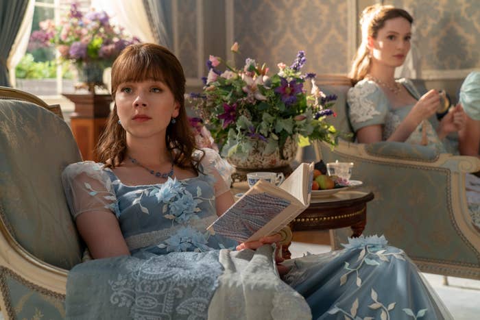 Eloise sitting and reading in a scene from &quot;Bridgerton&quot; with her sister Francesca in the background