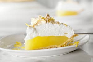 A slice of lemon meringue pie on a white plate, topped with fluffy meringue and lemon zest