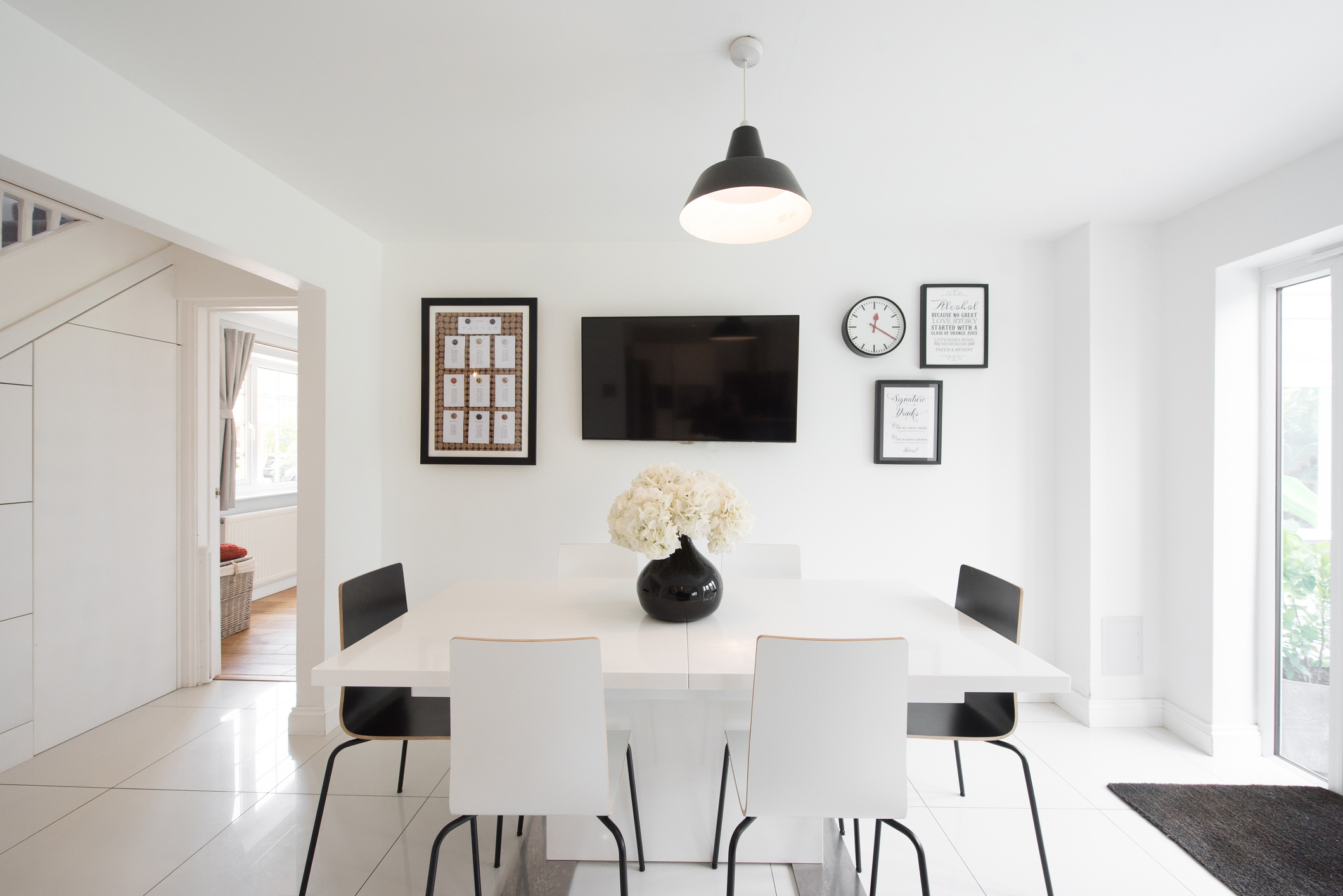 Modern dining room with a white table, four chairs, a black vase with flowers, and framed decor on the walls
