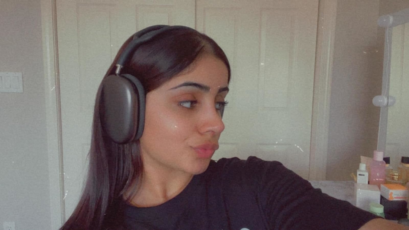 Seorang pengulas berpose di dalam ruangan dengan mengenakan headphone over-ear yang besar