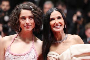 Margaret Qualley in a pink halter dress and Demi Moore in an off-shoulder gown smiling on a red carpet