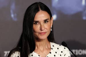 Demi Moore, wearing a polka dot blouse, is seen speaking at an event. She has long, straight hair and is looking slightly to the right of the camera