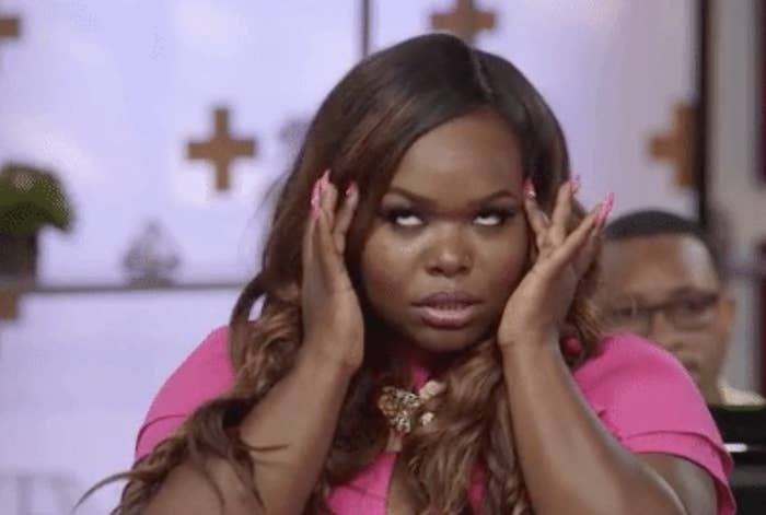 A woman with long hair and wearing a pink top rolls her eyes and holds her head with both hands in a gesture of frustration