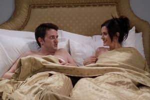 Matthew Perry and Courteney Cox in bed, covered by a blanket, sharing a humorous moment