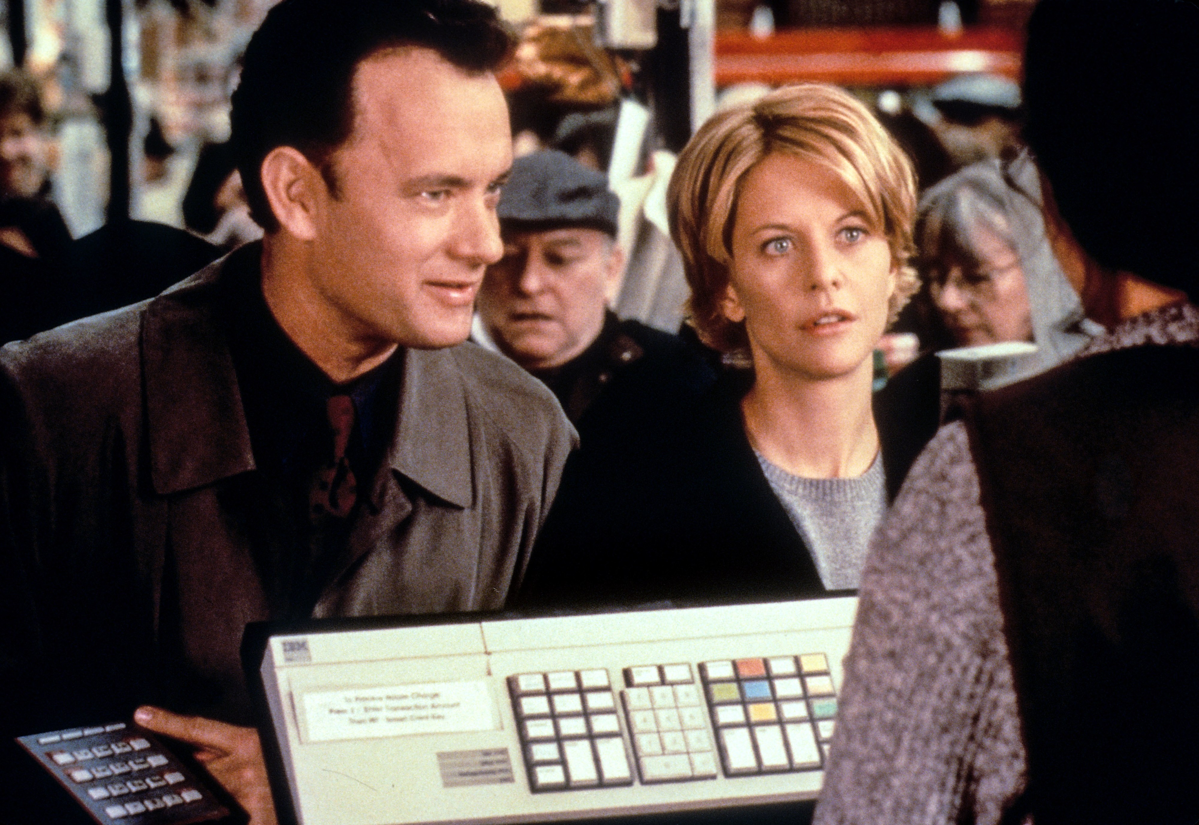 Tom Hanks and Meg Ryan stand at a store counter, looking at a clerk off-screen