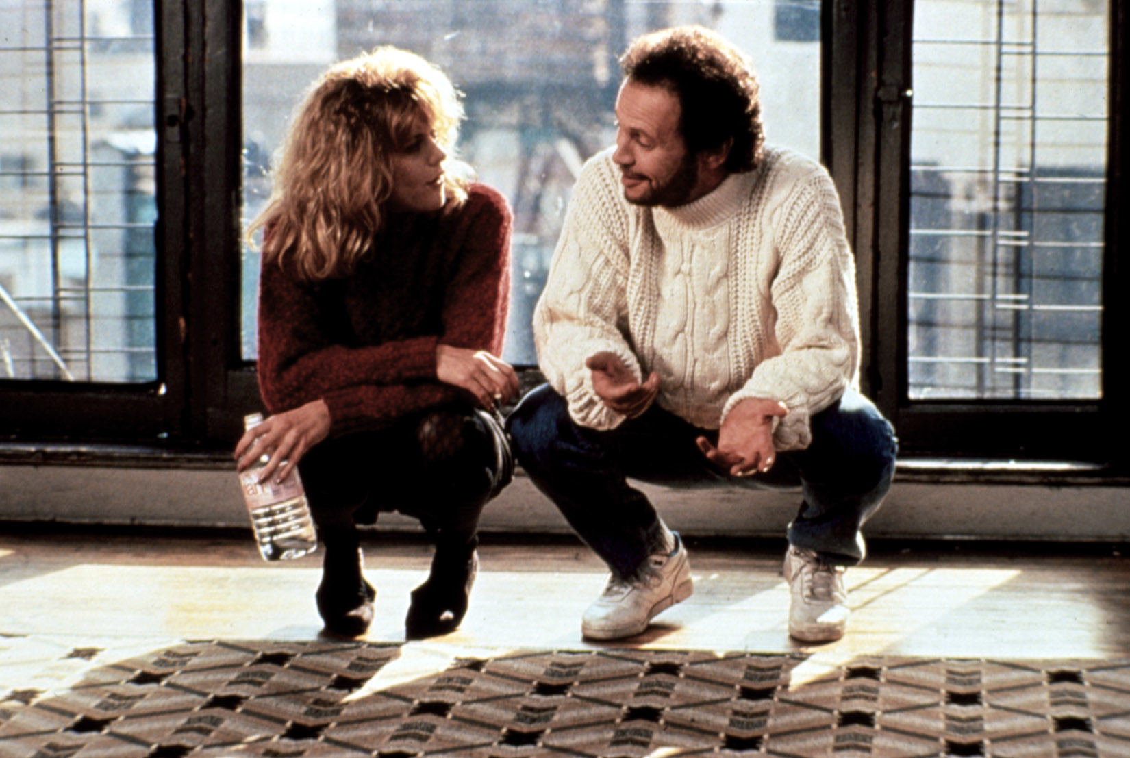 Meg Ryan and Billy Crystal crouching on the floor, deep in conversation, in a scene from "When Harry Met Sally." Ryan holds a water bottle