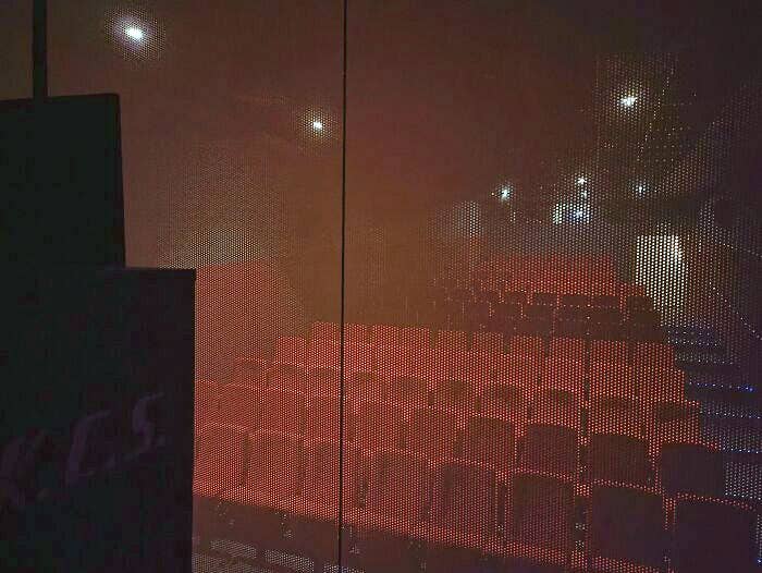Empty theater seating, viewed from behind a meshed screen, with dim lighting. No people present
