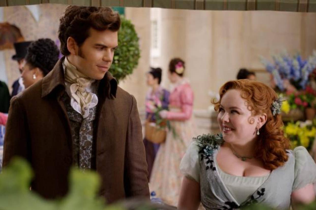 Nicola Coughlan and Luke Newton in period costumes with people in historical attire in the background