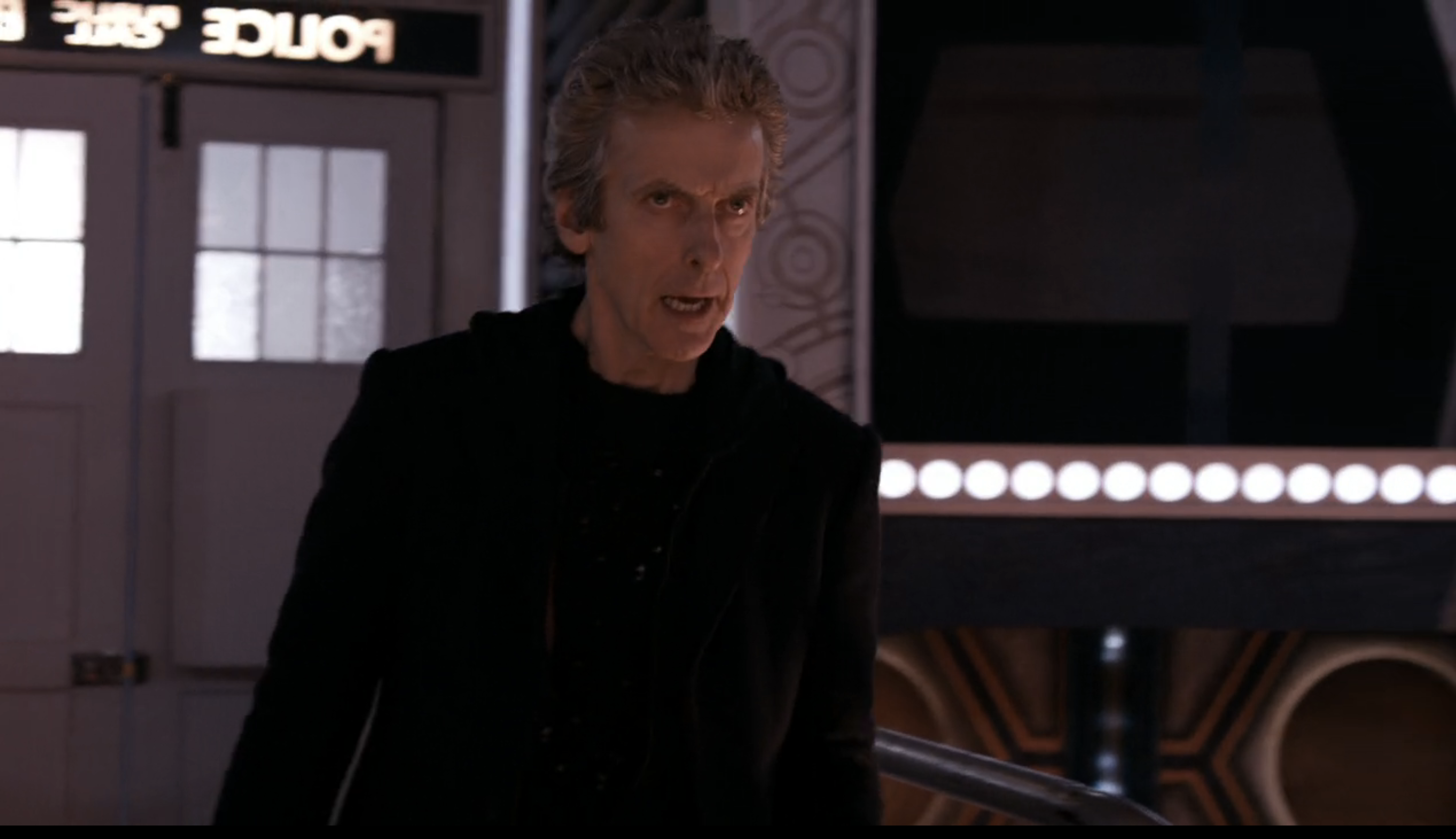 Peter Capaldi, dressed in a dark outfit, stands inside the TARDIS, looking intense and focused in a scene from "Doctor Who."