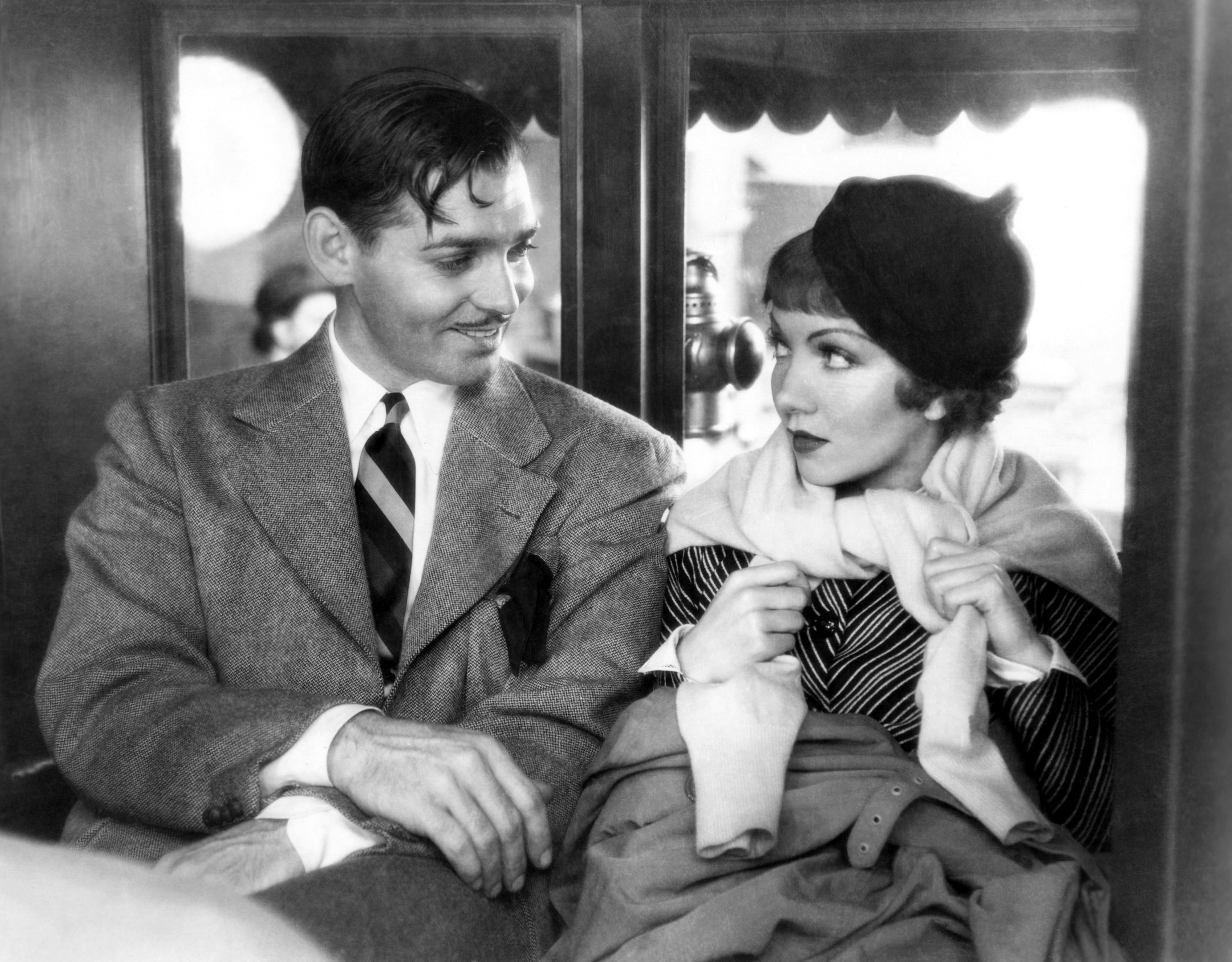 Clark Gable and Claudette Colbert sit together in a scene from the 1934 movie "It Happened One Night," both dressed in 1930s attire