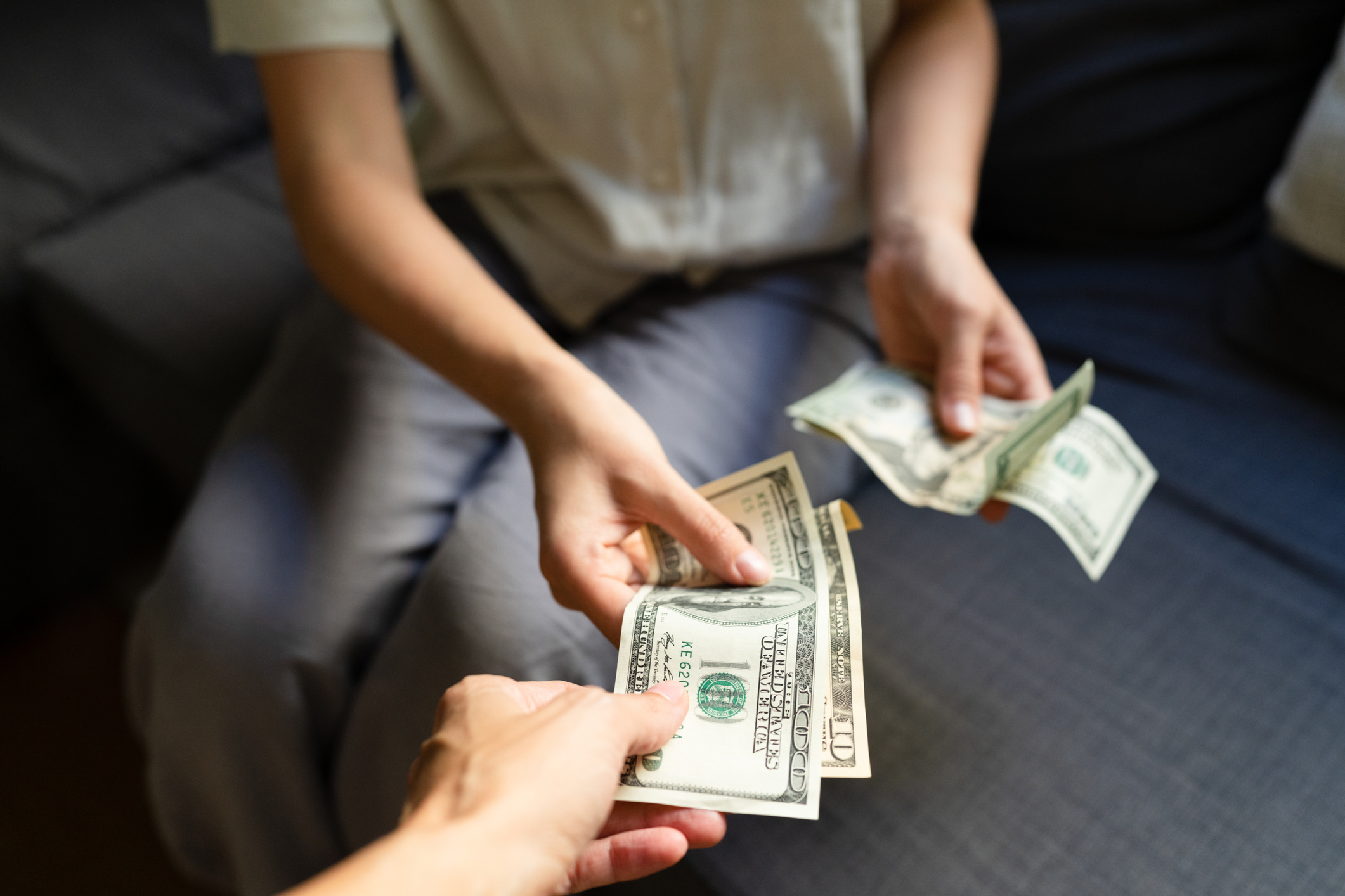 Two people exchanging US dollar bills, one person handing cash to the other