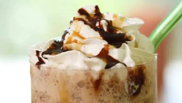 A close-up of a decadent milkshake topped with whipped cream, chocolate, and caramel drizzle, with a green straw