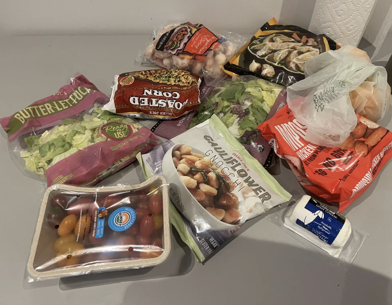 Fresh groceries on a kitchen counter include lettuce, tomatoes, assorted vegetables, pasta, and cheese