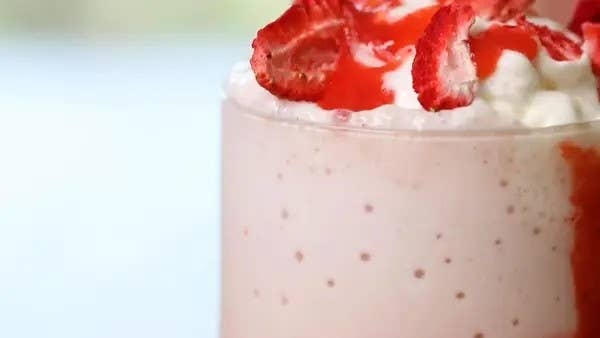 A close-up of a strawberry milkshake topped with whipped cream and sliced strawberries, highlighting its creamy texture and fresh fruit garnish