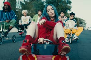 Billie Eilish drives a small car with several people on small bikes in the background in the Bad Guy music video