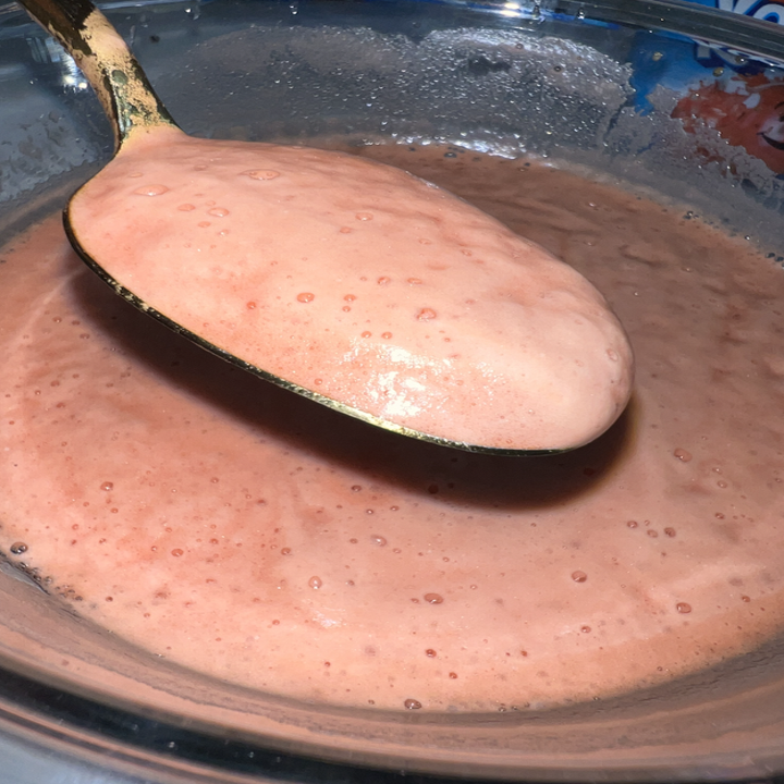 A close-up image of a spoon scooping bubbly pinkish batter from a bowl. The texture appears smooth and creamy. This image is related to food