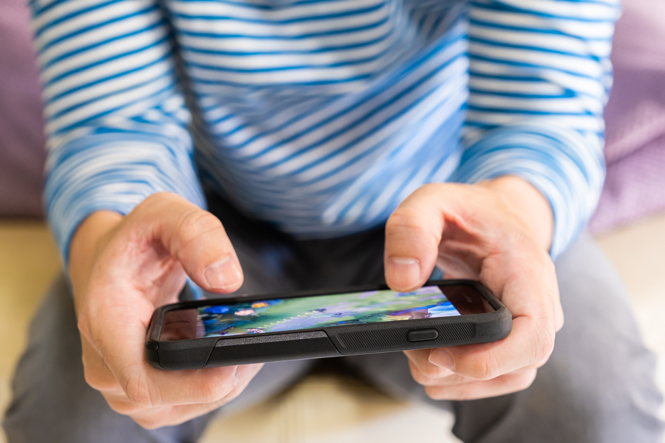 Person in a striped shirt holding a smartphone, focused on the device's screen. The image captures their hands and part of their torso