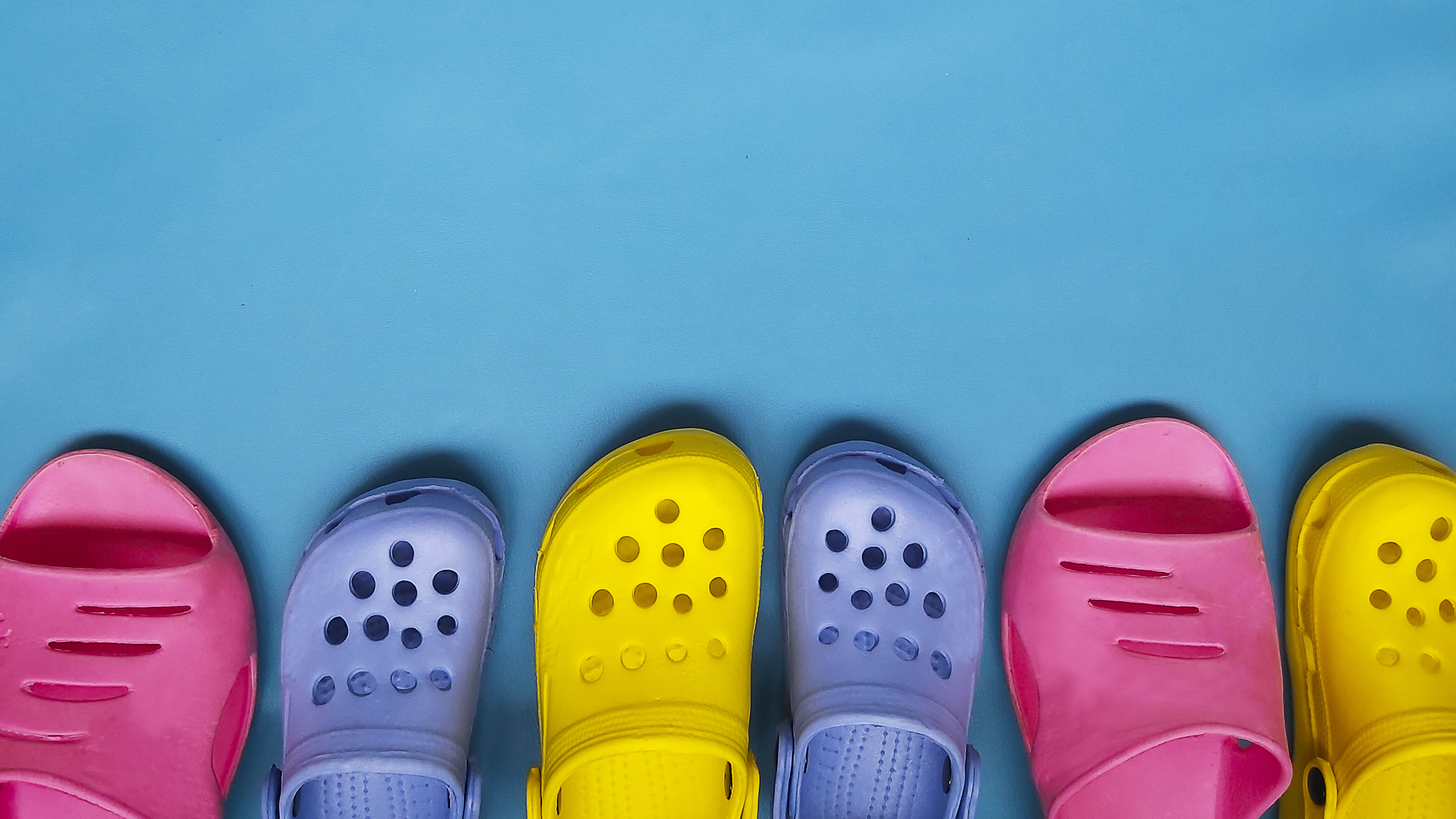 Five pairs of colorful Crocs shoes are arranged in a row on a blue background