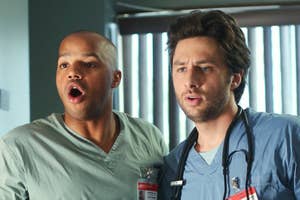 Donald Faison and Zach Braff, dressed as doctors, stand side by side with surprised expressions in a scene from the TV show Scrubs