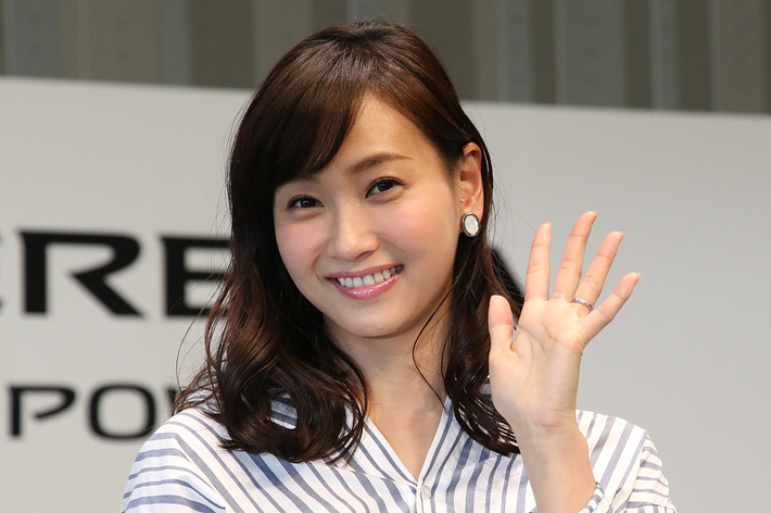 芸能人のユミ・アドリアーナがストライプ模様のドレスを着て、カメラに向かって手を振って微笑んでいます。