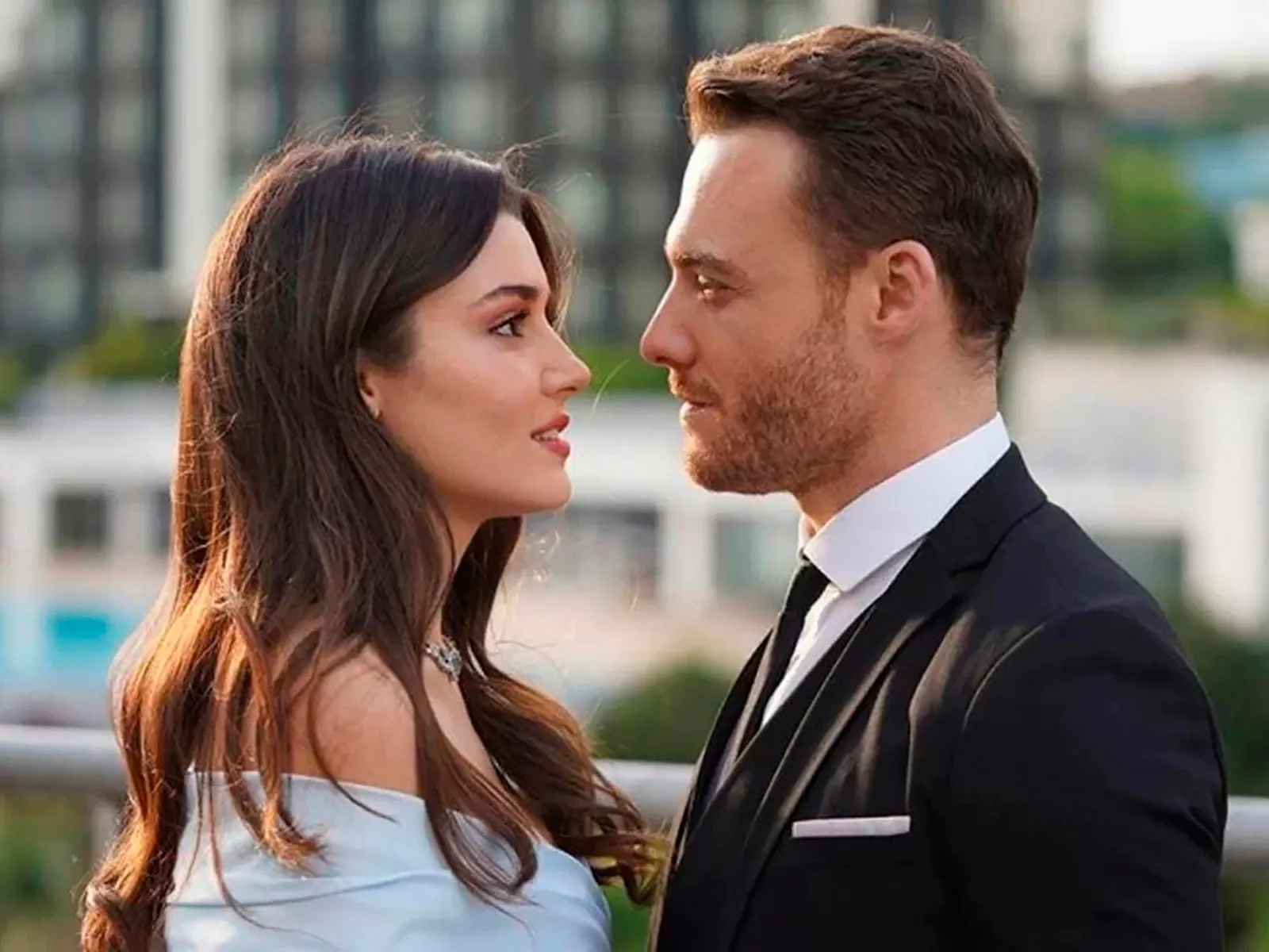 Hande Erçel y Kerem Bürsin mirándose frente a frente, Hande viste un elegante vestido mientras Kerem lleva un traje formal