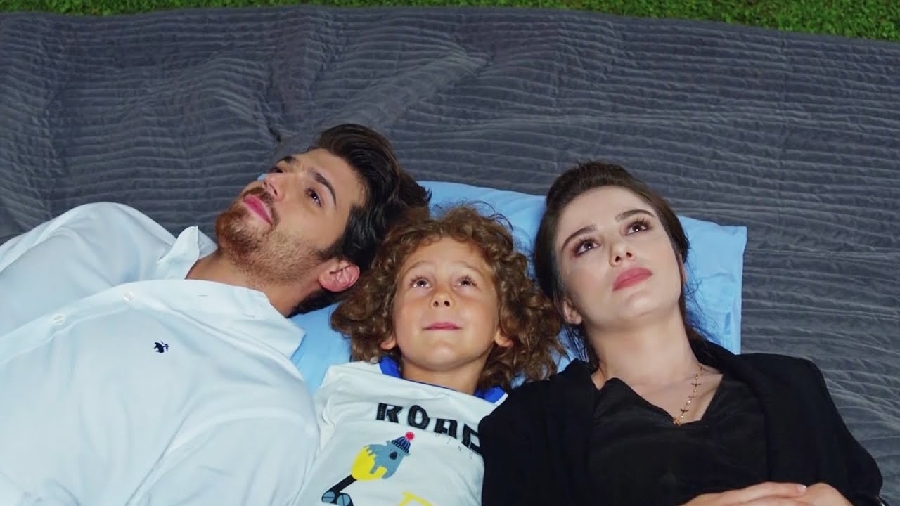 Tres personas están recostadas en el césped mirando hacia arriba: una mujer, un hombre y un niño. Todos parecen pensativos y relajados