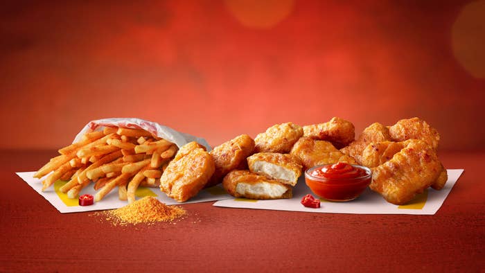 A serving of fries and chicken nuggets with a side of ketchup arranged on a red surface with a red-orange background. A small pile of seasoning is next to the fries