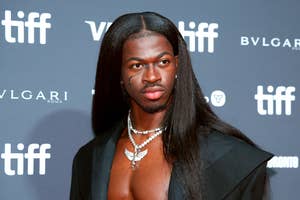 Lil Nas X on the red carpet at the Toronto International Film Festival, wearing an open black jacket showcasing a diamond necklace with an intricate design