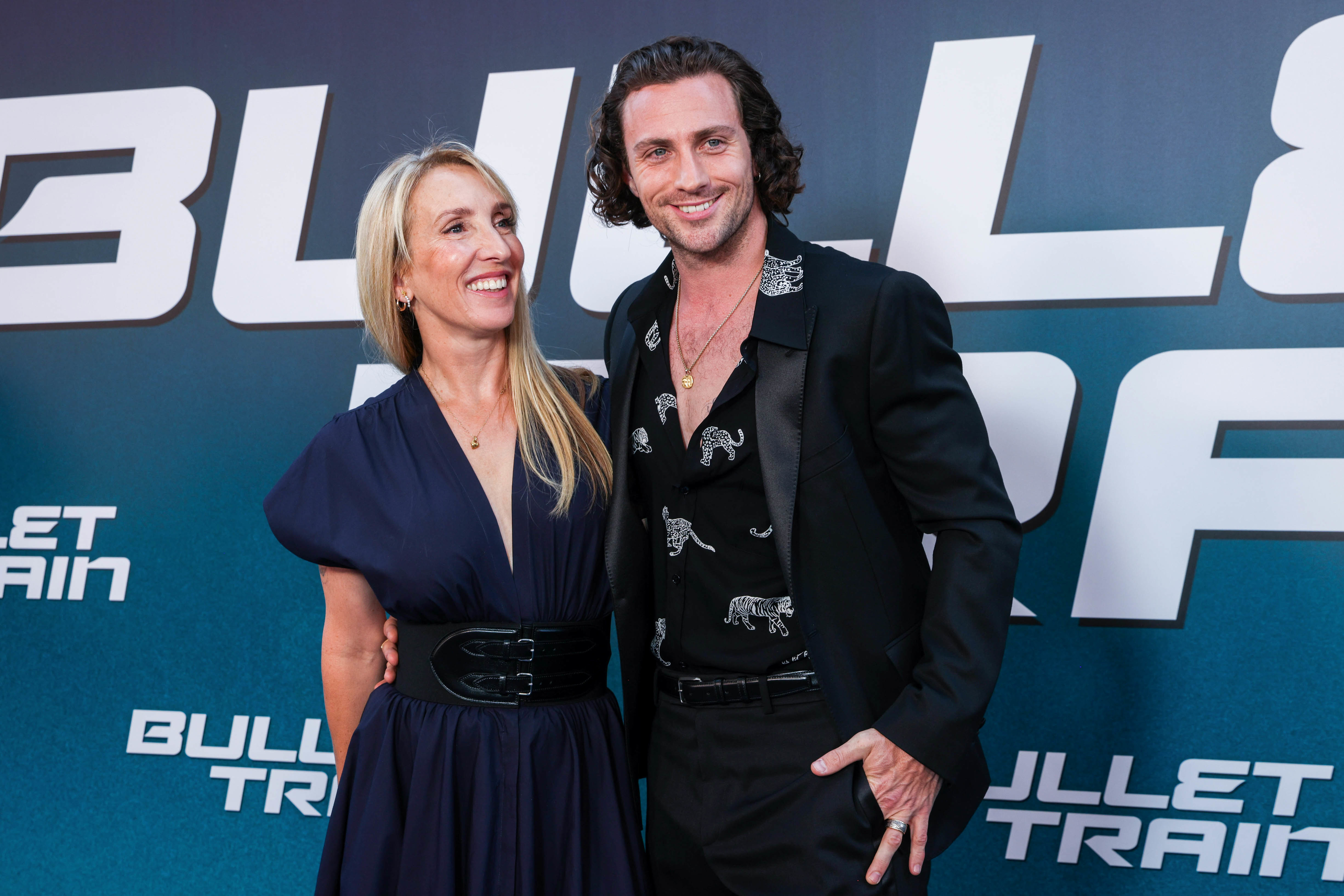 Sam Taylor-Johnson in a belted dress and Aaron Taylor-Johnson in a dark suit pose together at the Bullet Train premiere