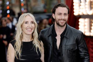 Sam Taylor-Johnson wearing a sleeveless dress and Aaron Taylor-Johnson in a leather jacket, smiling on the red carpet