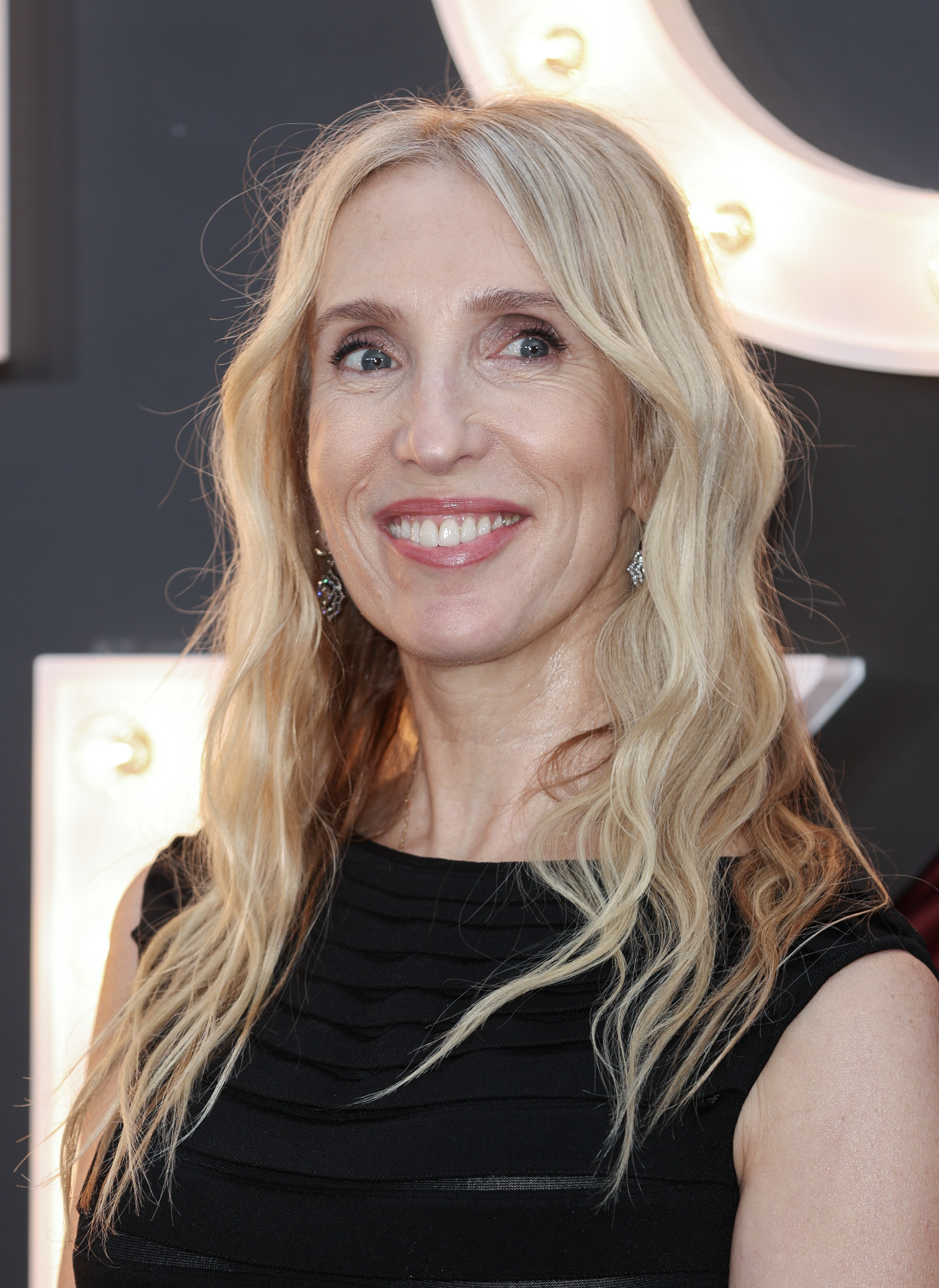 Sam Taylor-Johnson smiling on the red carpet, wearing a sleeveless dress with wavy hair