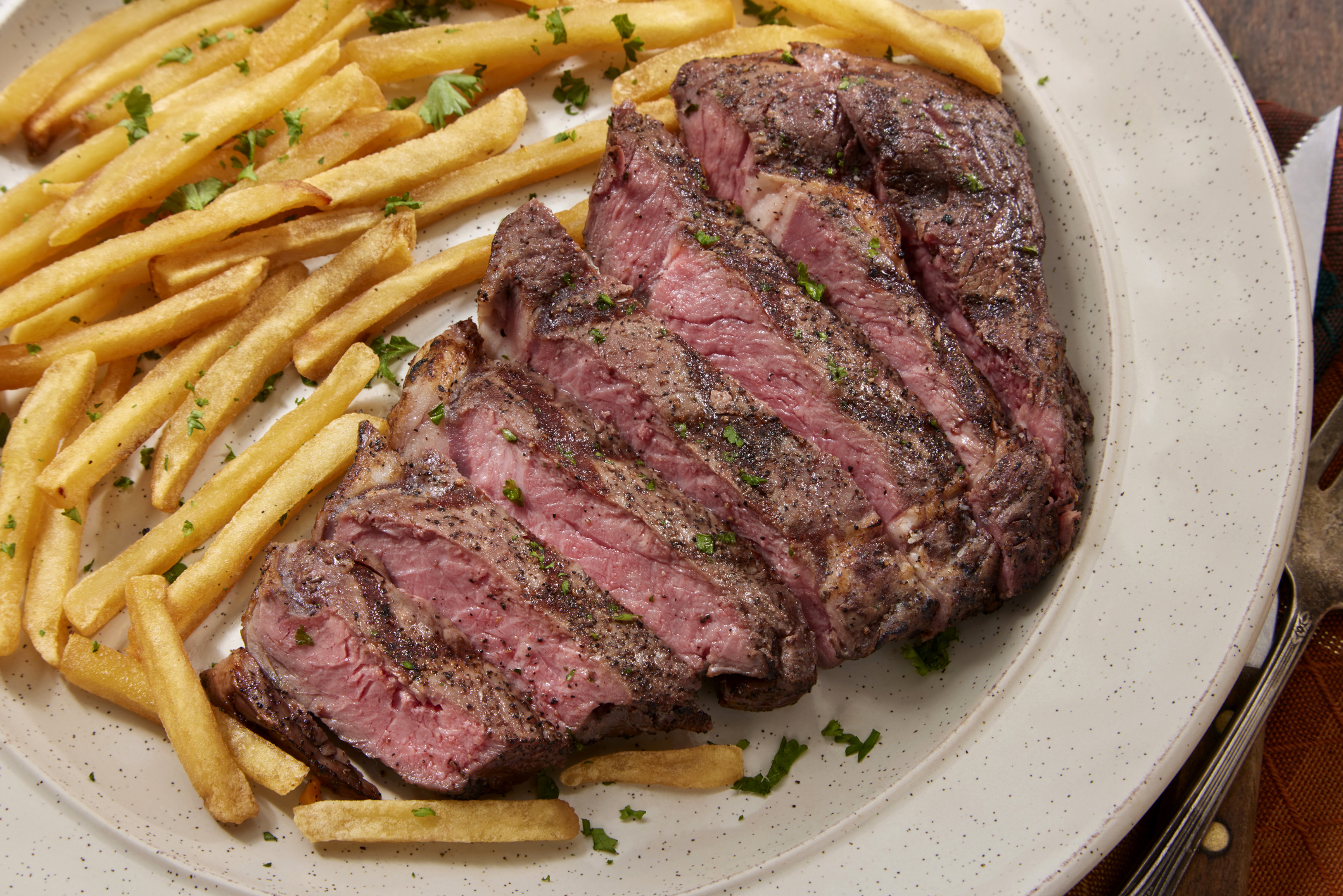 A plate of sliced steak alongside seasoned fries garnished with parsley