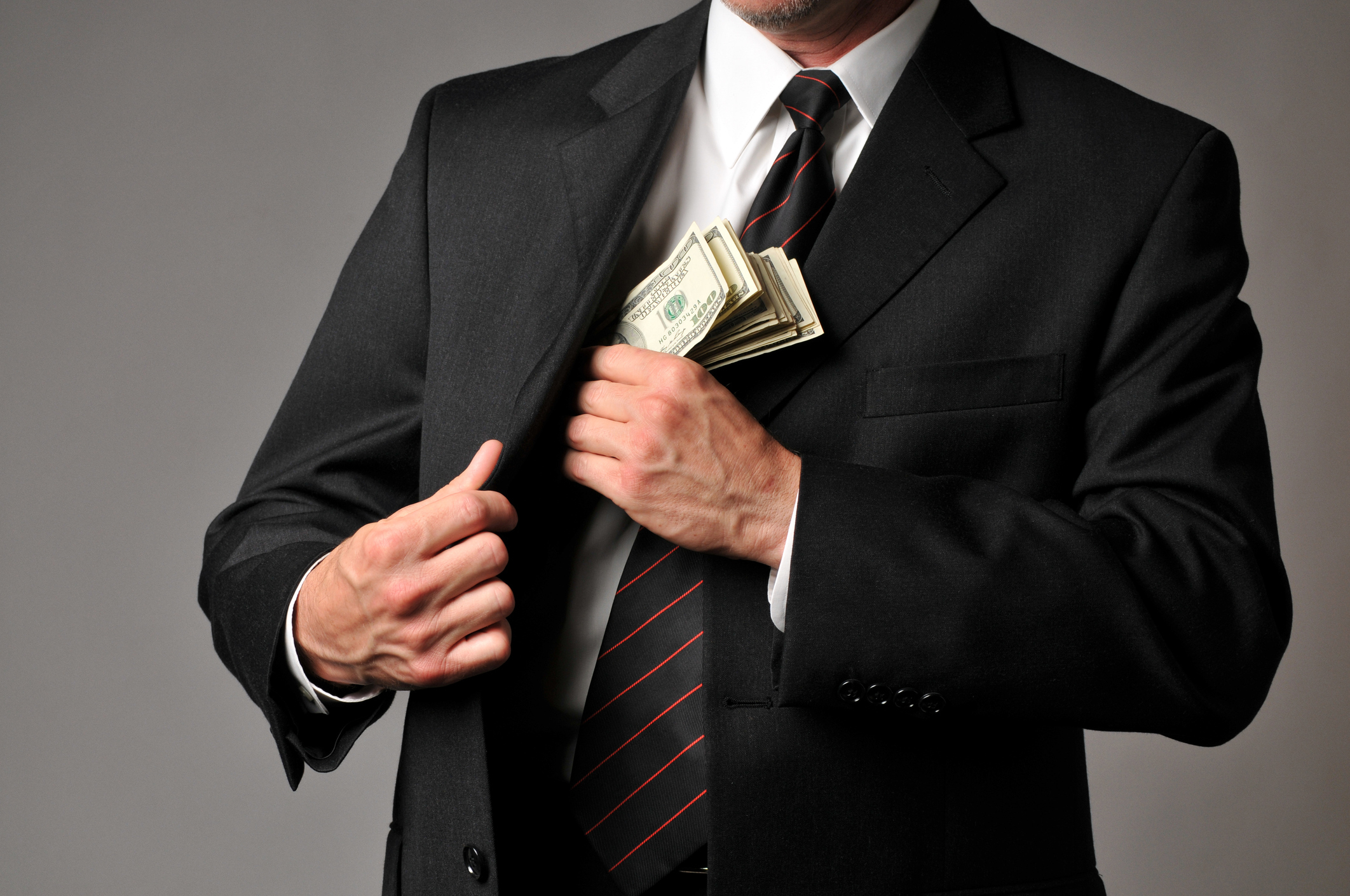 A man in a suit and tie puts a stack of money into his jacket pocket