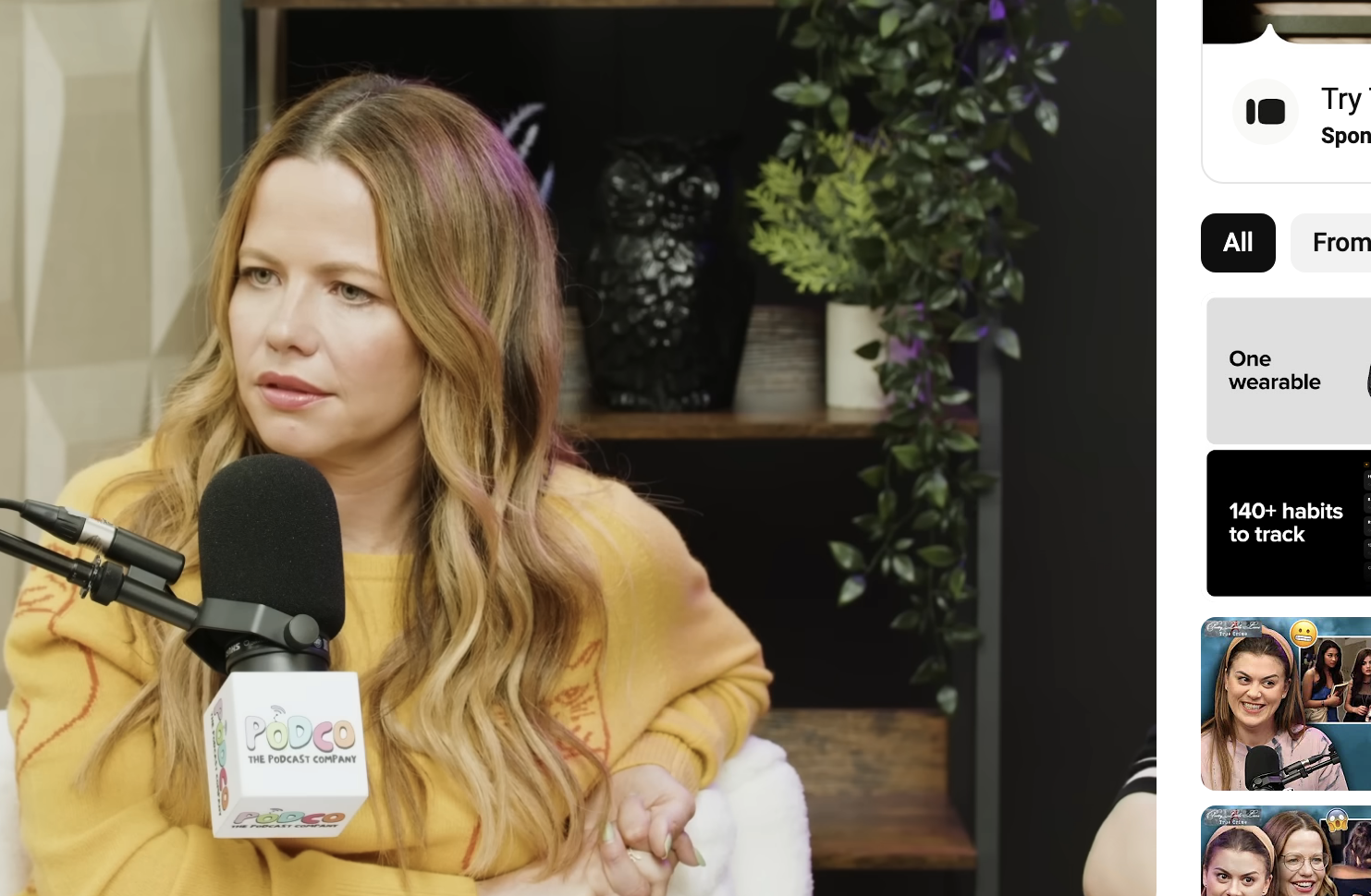 Sasha Pieterse speaks into a microphone during an interview on Pretty Little Liars: True Crime YouTube show. She is wearing a long-sleeve top