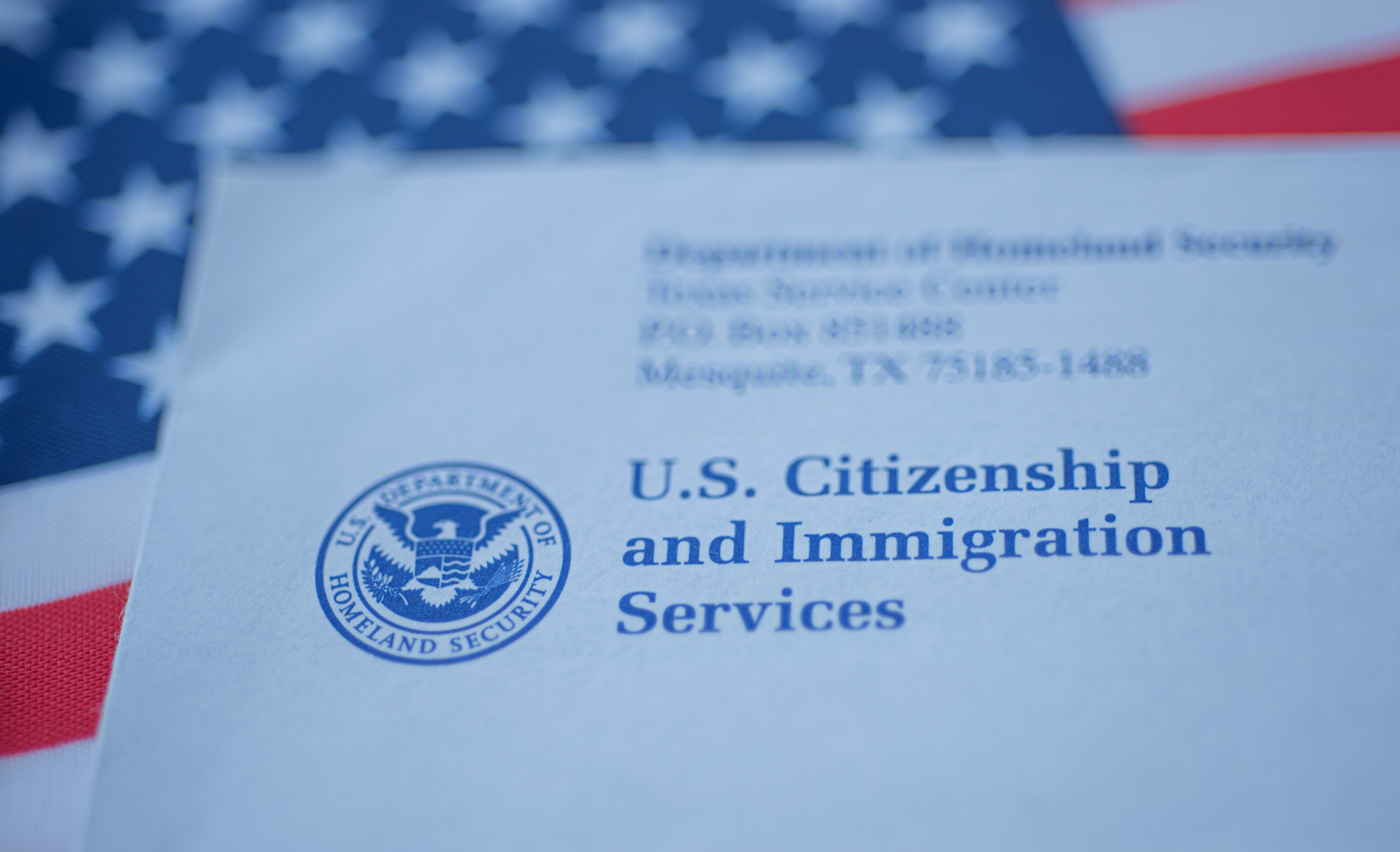 Close-up of a U.S. Citizenship and Immigration Services document with a blurred American flag in the background