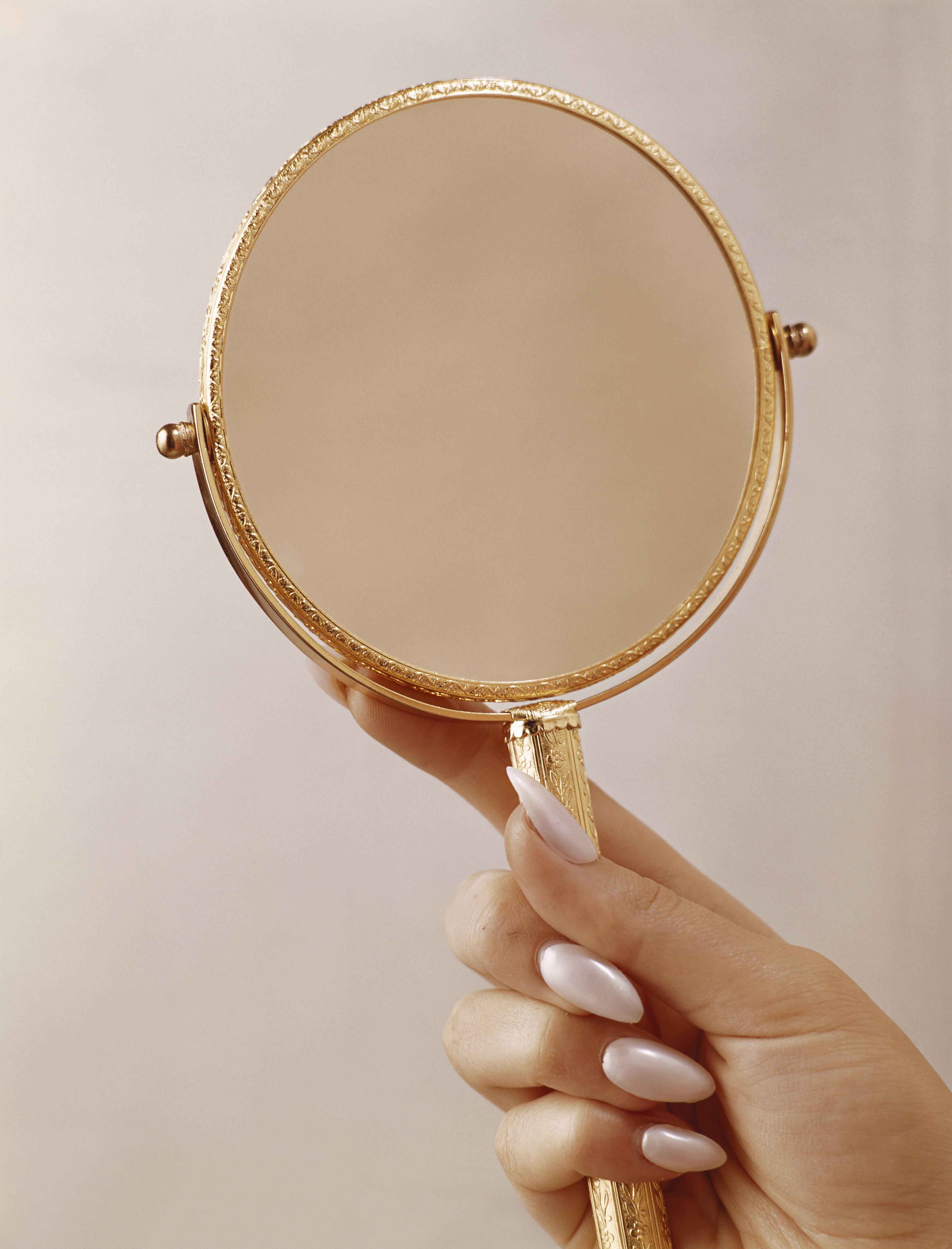 Hand holding an ornate round mirror with delicate detailing on the gold handle and frame