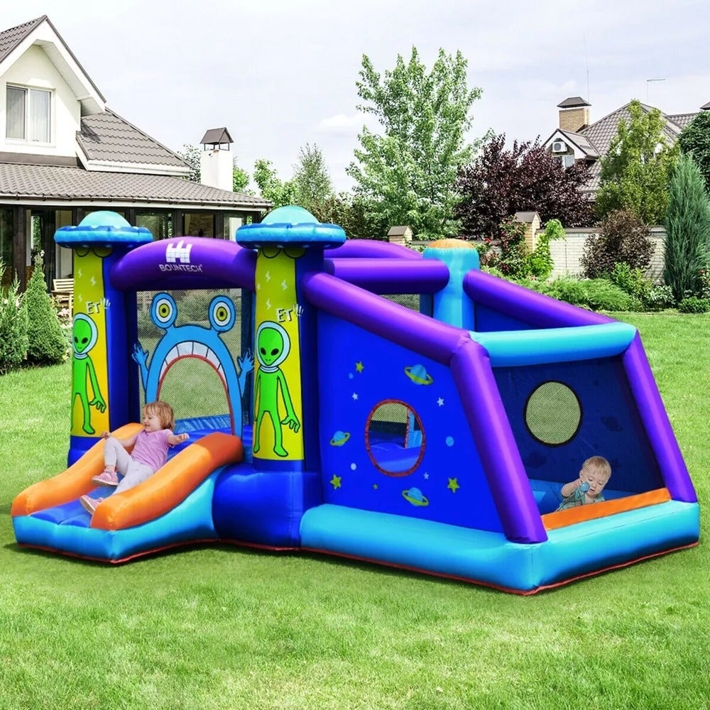 Dua anak bermain di rumah bouncing tiup bertema alien dengan perosotan dan lubang bola
