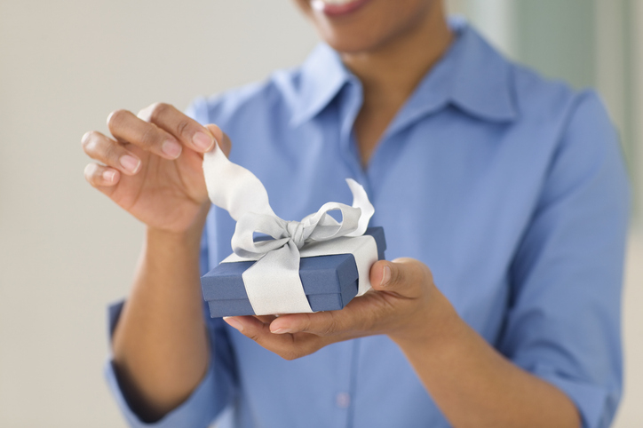 A person in a blue shirt is unwrapping a ribbon from a small gift box. The image is used in an article categorized as Sex &amp;amp; Love