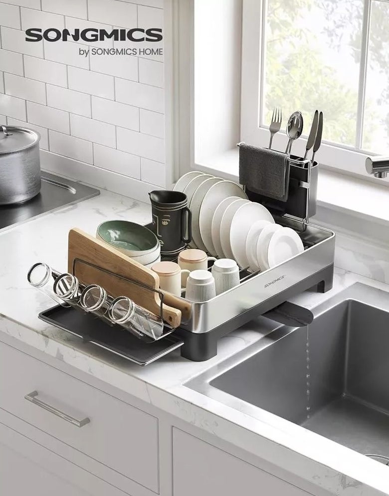 Rak pengering piring SONGMICS dengan piring, mangkok, cangkir, talenan, perkakas, dan peralatan dapur tersusun rapi di meja dapur di sebelah wastafel