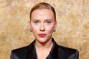 Scarlett Johansson wearing a sleek black jacket with her hair slicked back in front of a textured backdrop