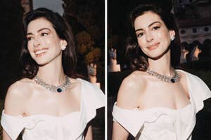 Anne Hathaway in an elegant white off-shoulder gown, adorned with a statement necklace, smiling and posing at an outdoor event